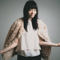 ベージュの羽織を肩に掛けて腕を広げてほくそ笑む女性の写真