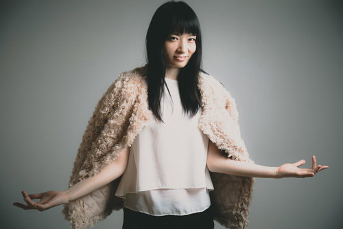 ベージュの羽織を肩に掛けて腕を広げてほくそ笑む女性