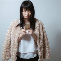 スマホを見て不機嫌になるベージュカーディガンを羽織る女性の写真