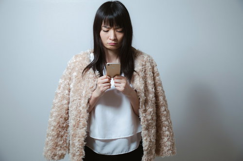 スマホを見て不機嫌になるベージュカーディガンを羽織る女性
