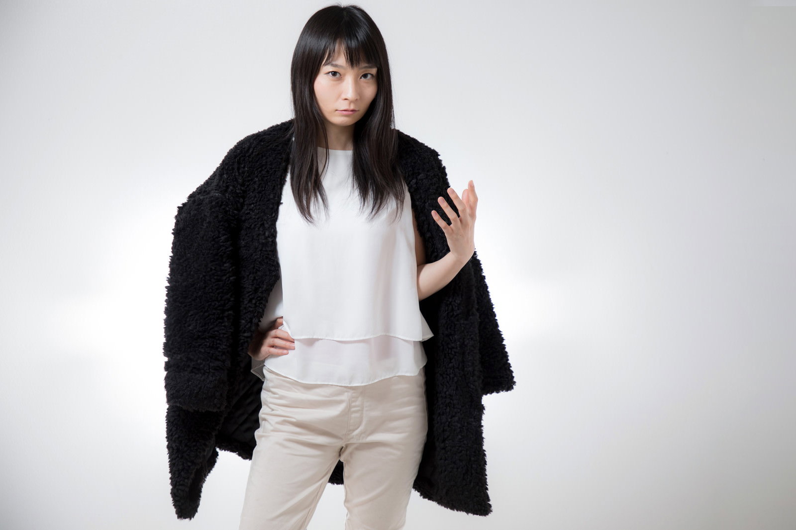 黒いジャケットを肩に掛け片手を腰に当ててミンゴ立ちする女性［モデル：たけべともこ］