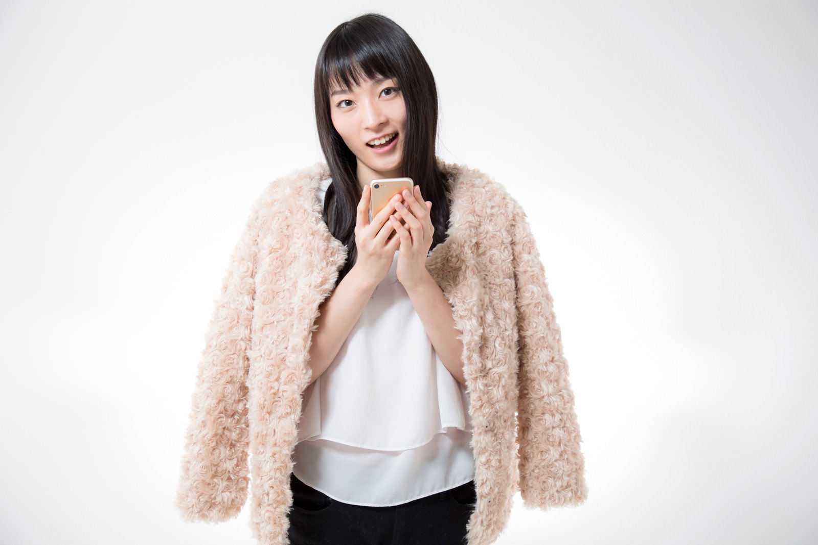ベージュのファー調アウターを着た黒髪ボブの女性がスマホを両手で抱えて微笑んでいる［モデル：たけべともこ］