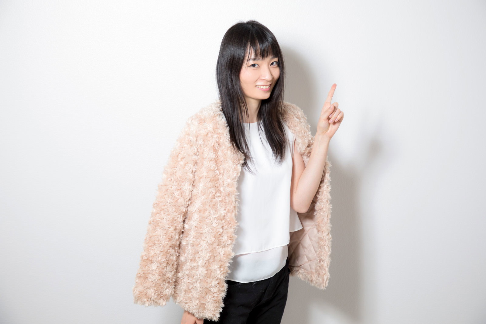 ベージュのカーディガンを着た女性が人差し指を立てて笑顔でポーズ［モデル：たけべともこ］
