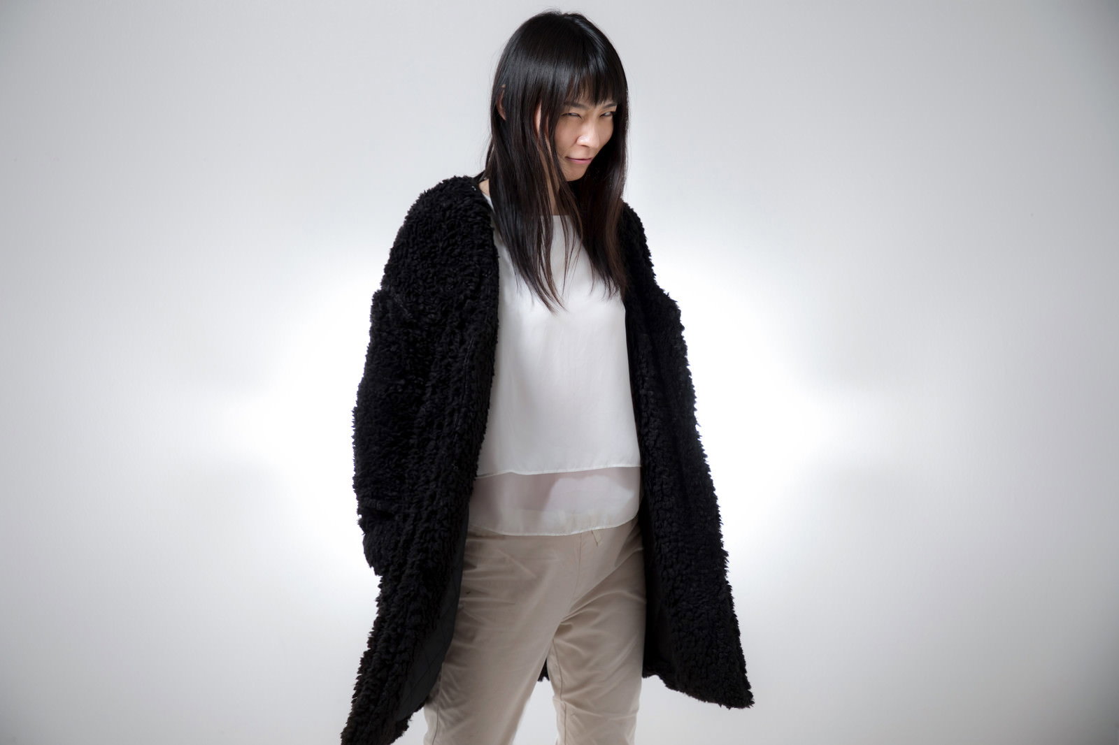 黒い服を着た長髪の女性がほくそ笑みながらカメラを見つめる［モデル：たけべともこ］