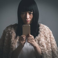 フード被ってスマホ越しに睨む不機嫌な女性の写真