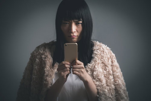 フード被ってスマホ越しに睨む不機嫌な女性