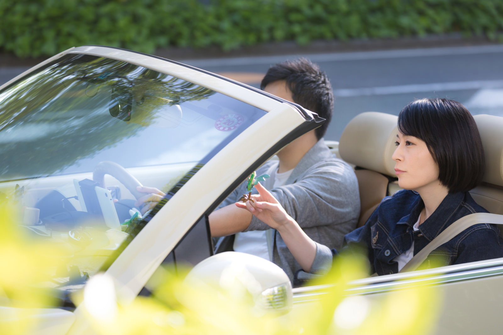 緑の道路を走るオープンカーでドライブを楽しむ若い男女のカップル［モデル：たけべともこ］