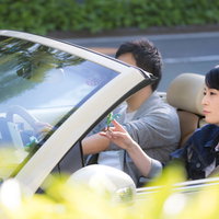 緑の道路を走るオープンカーでドライブを楽しむ若い男女の写真