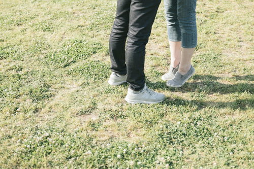 芝生で背伸びする彼女の足元、寄り添うカップルの恋愛シーン