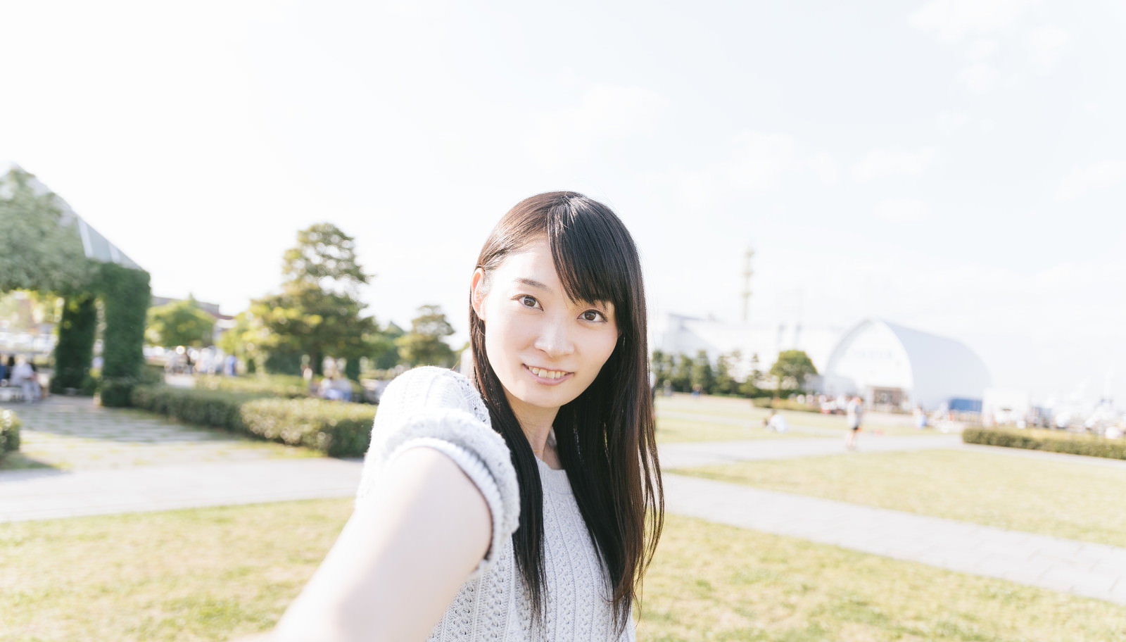 白いニットカーディガンを着た女性が公園で振り返り、笑顔で招く仕草をしている［モデル：たけべともこ］