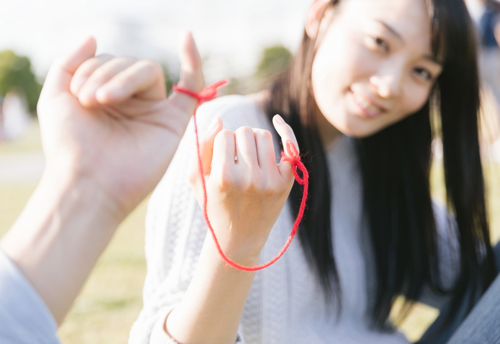 小指に赤い糸を結んだカップルの手元を撮影した写真［モデル：たけべともこ］