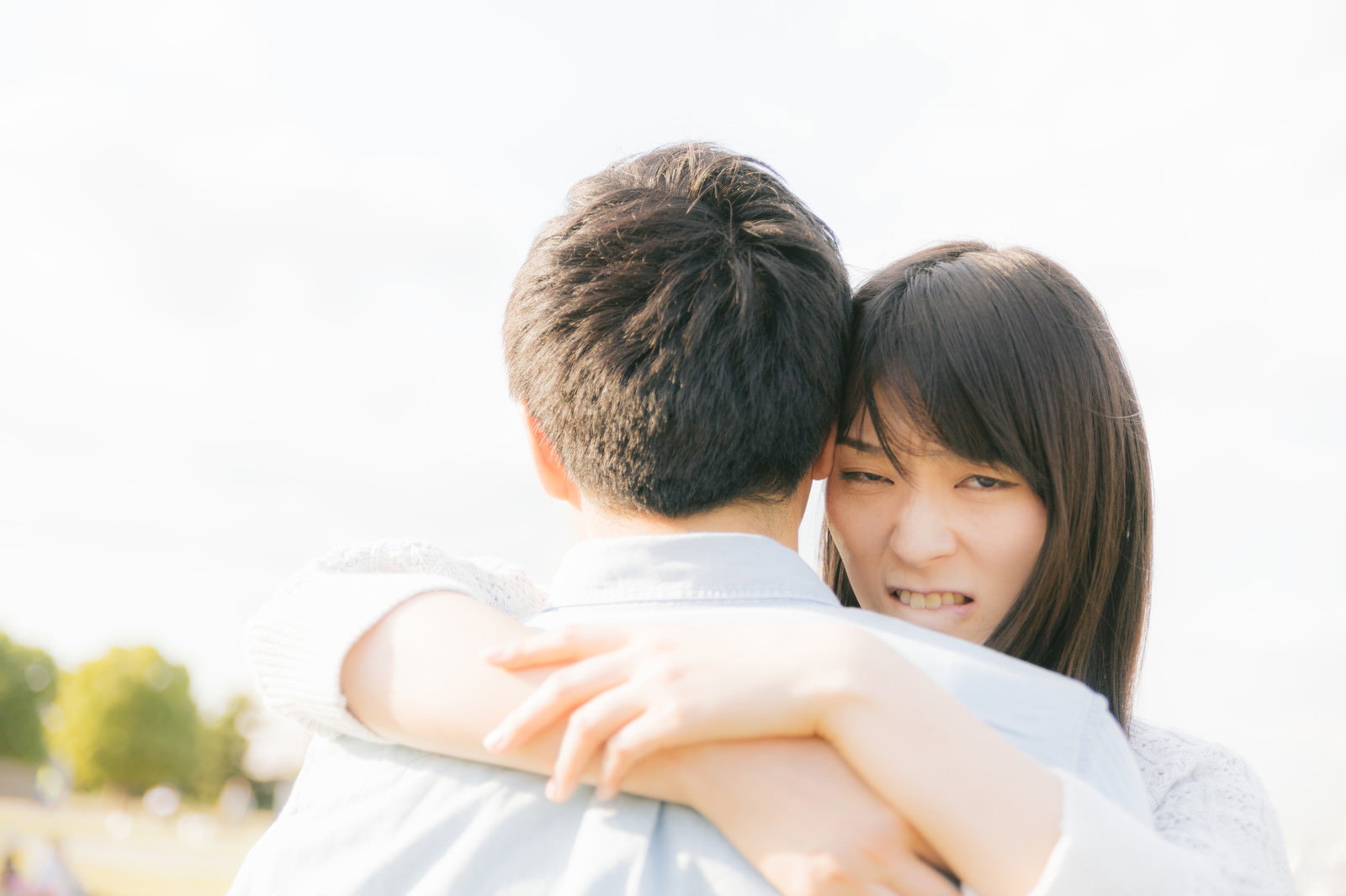 不機嫌そうな表情を見せながら男性にハグする女性とカップル［モデル：たけべともこ］