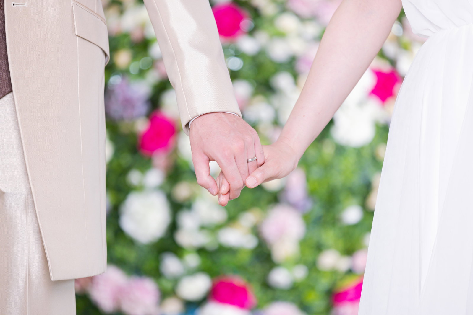 白いドレスの新婦と新郎が手を握り合い、結婚指輪が見える［モデル：たけべともこ］