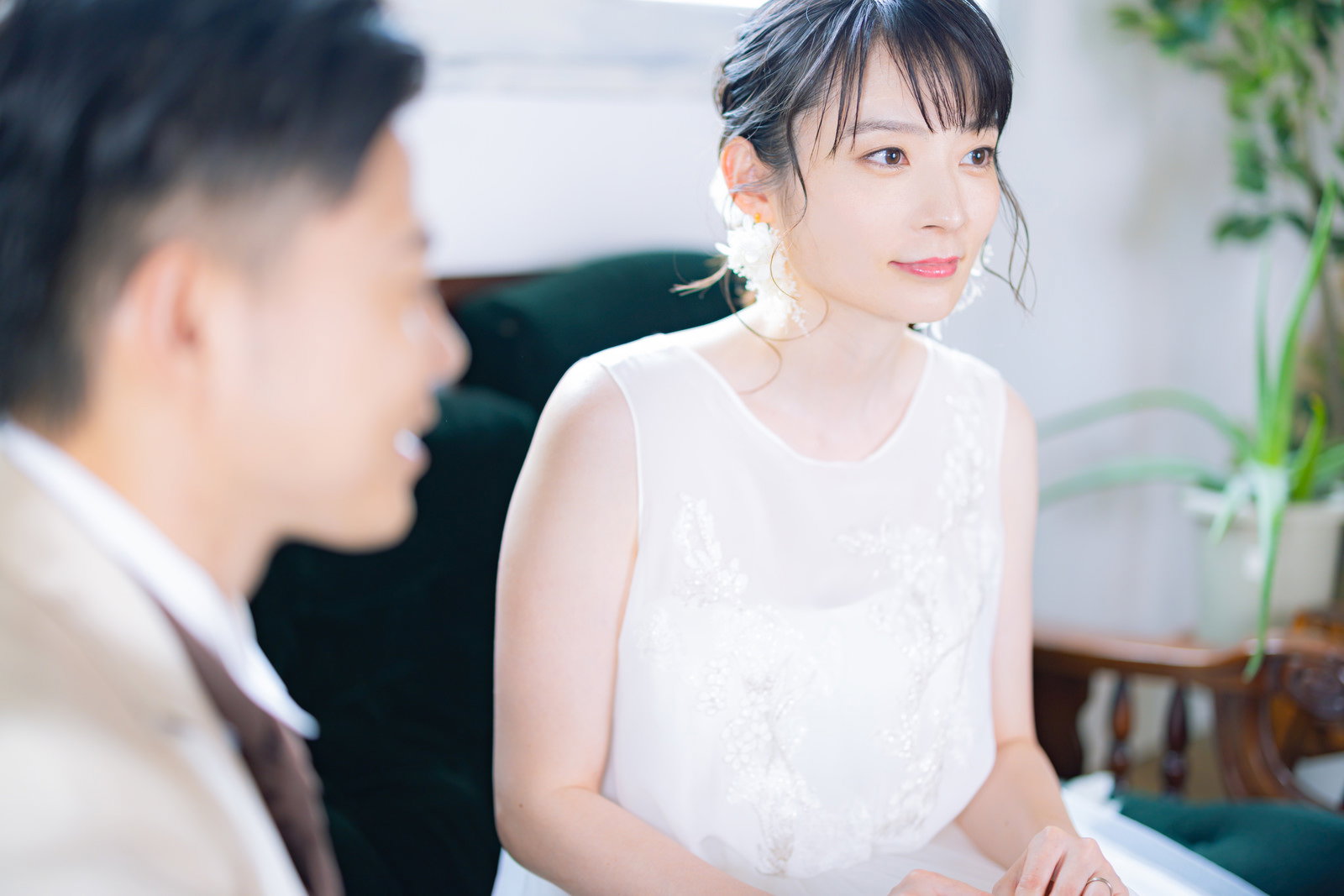 白いウェディングドレスを着た笑顔の新婦と隣に座る新郎［モデル：たけべともこ］