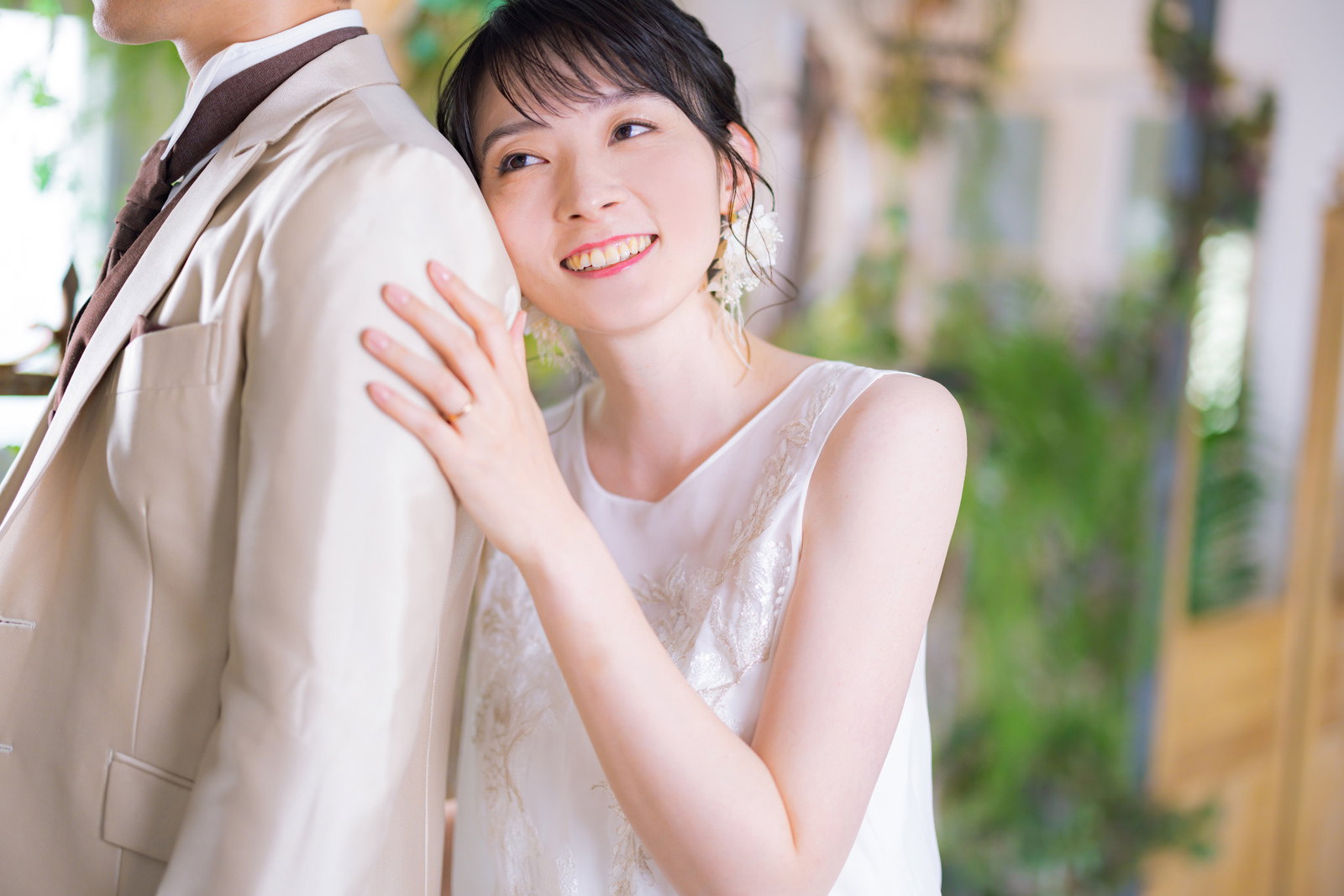 白いウェディングドレスを着た新婦が新郎の背中に寄り掛かっている様子［モデル：たけべともこ］