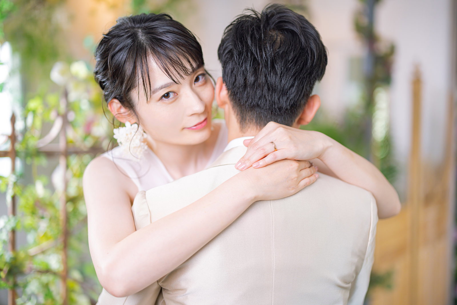 白いウェディングドレスを着た新婦が新郎を優しく抱きしめている［モデル：たけべともこ］
