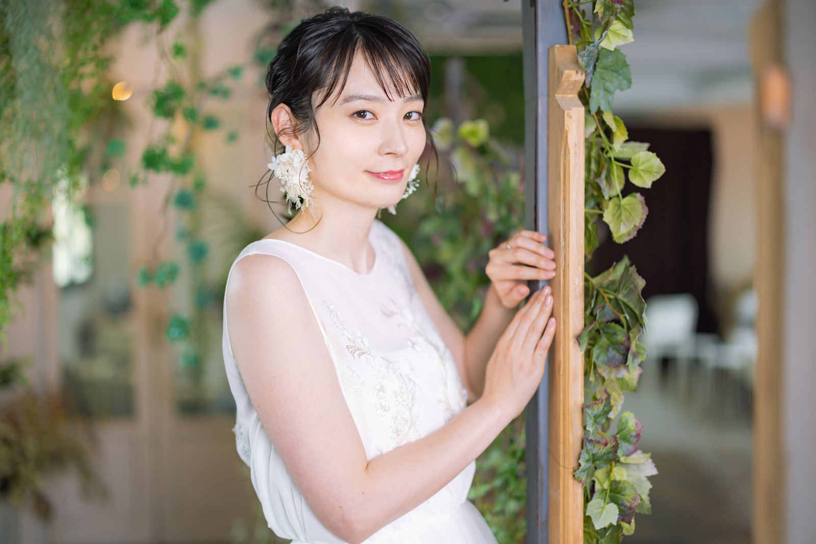 白いウェディングドレスを着て柱に手を添えて微笑む女性［モデル：たけべともこ］