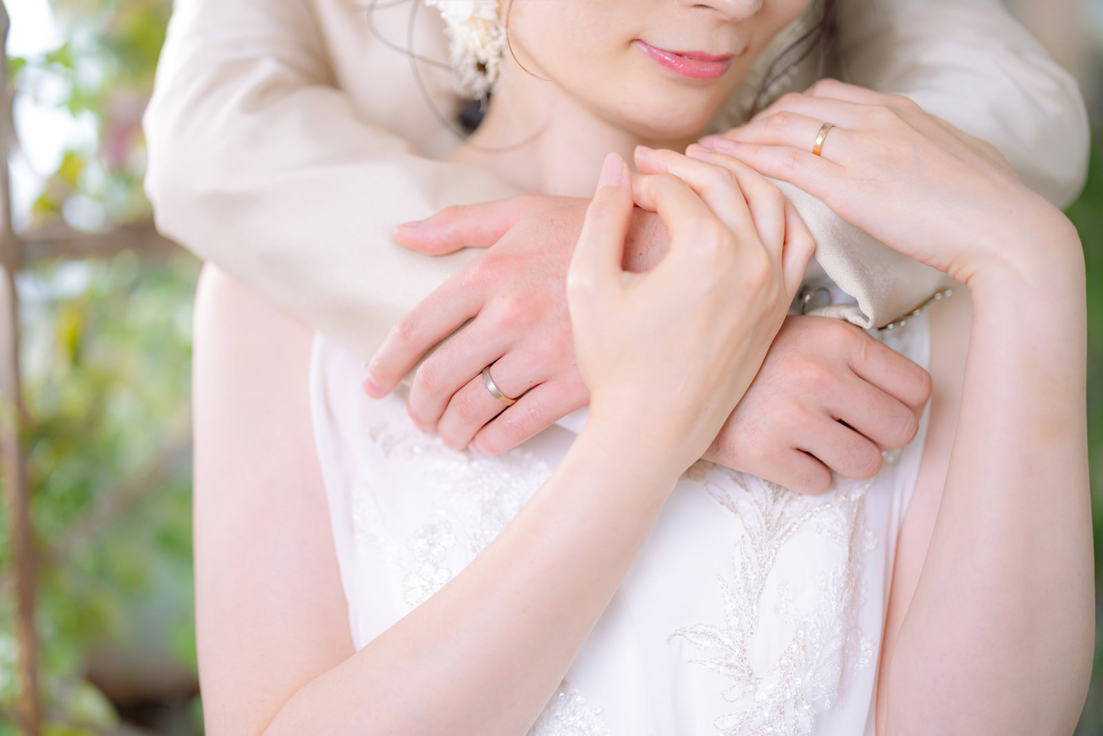 白いウェディングドレス姿の新婦が新郎に抱きしめられている様子［モデル：たけべともこ］