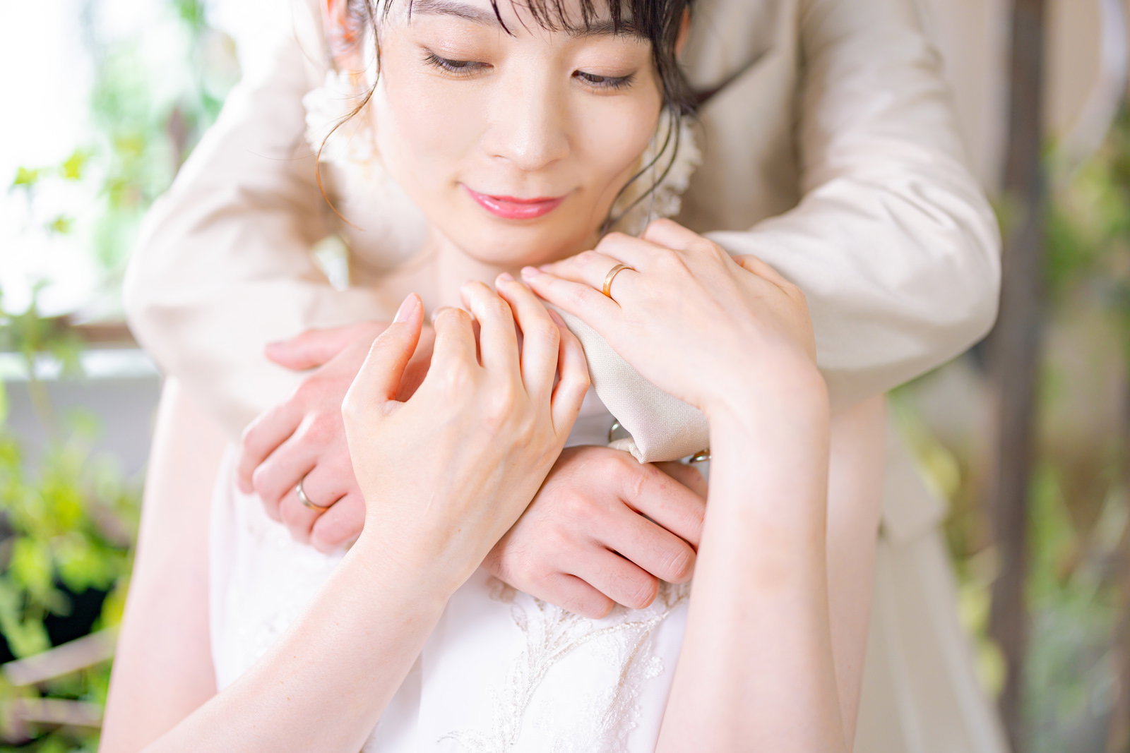 白いウェディングドレス姿の新婦が新郎に後ろから抱きしめられている［モデル：たけべともこ］