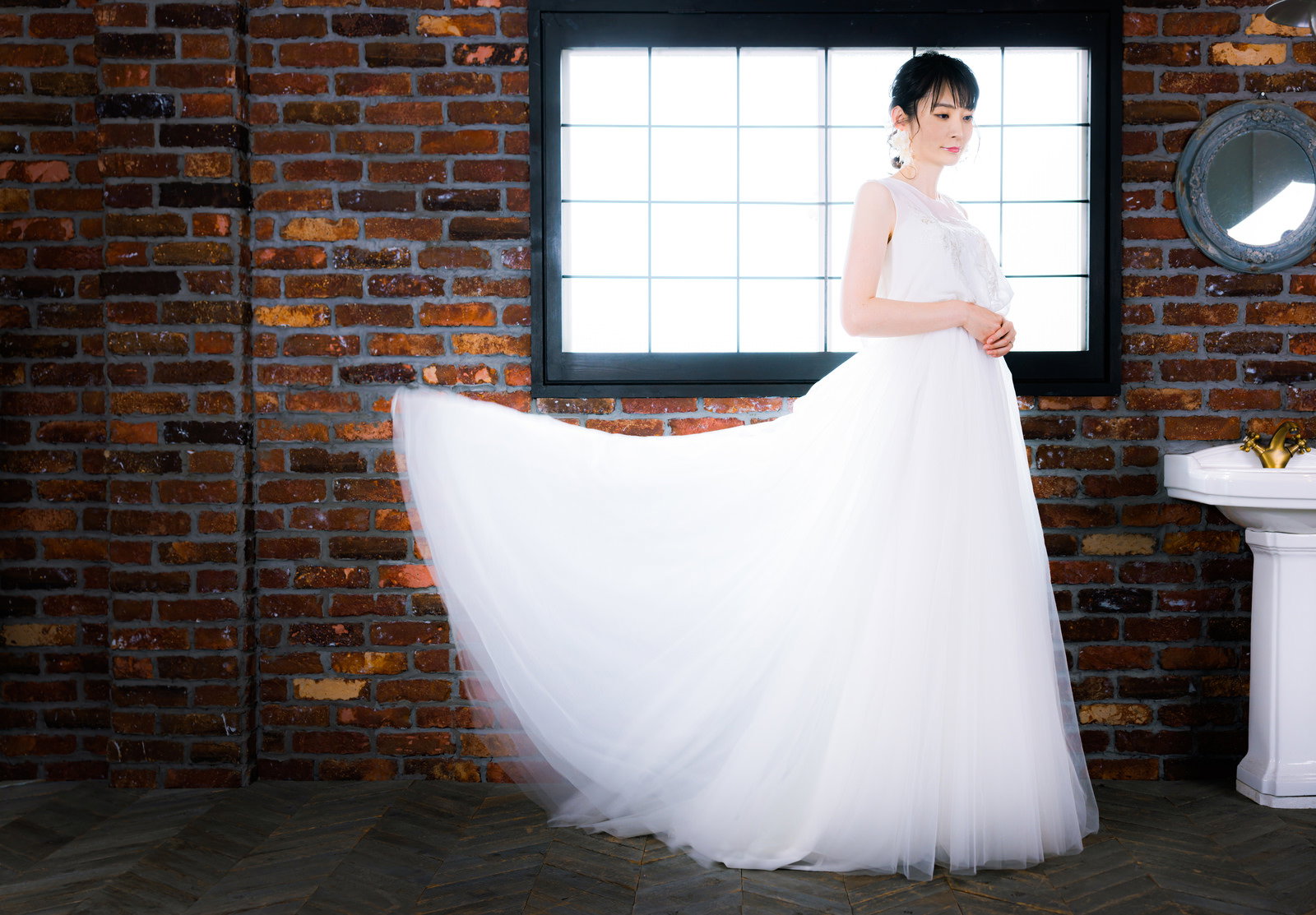 白いウェディングドレスを着た新婦がレンガの壁の前に立っている［モデル：たけべともこ］