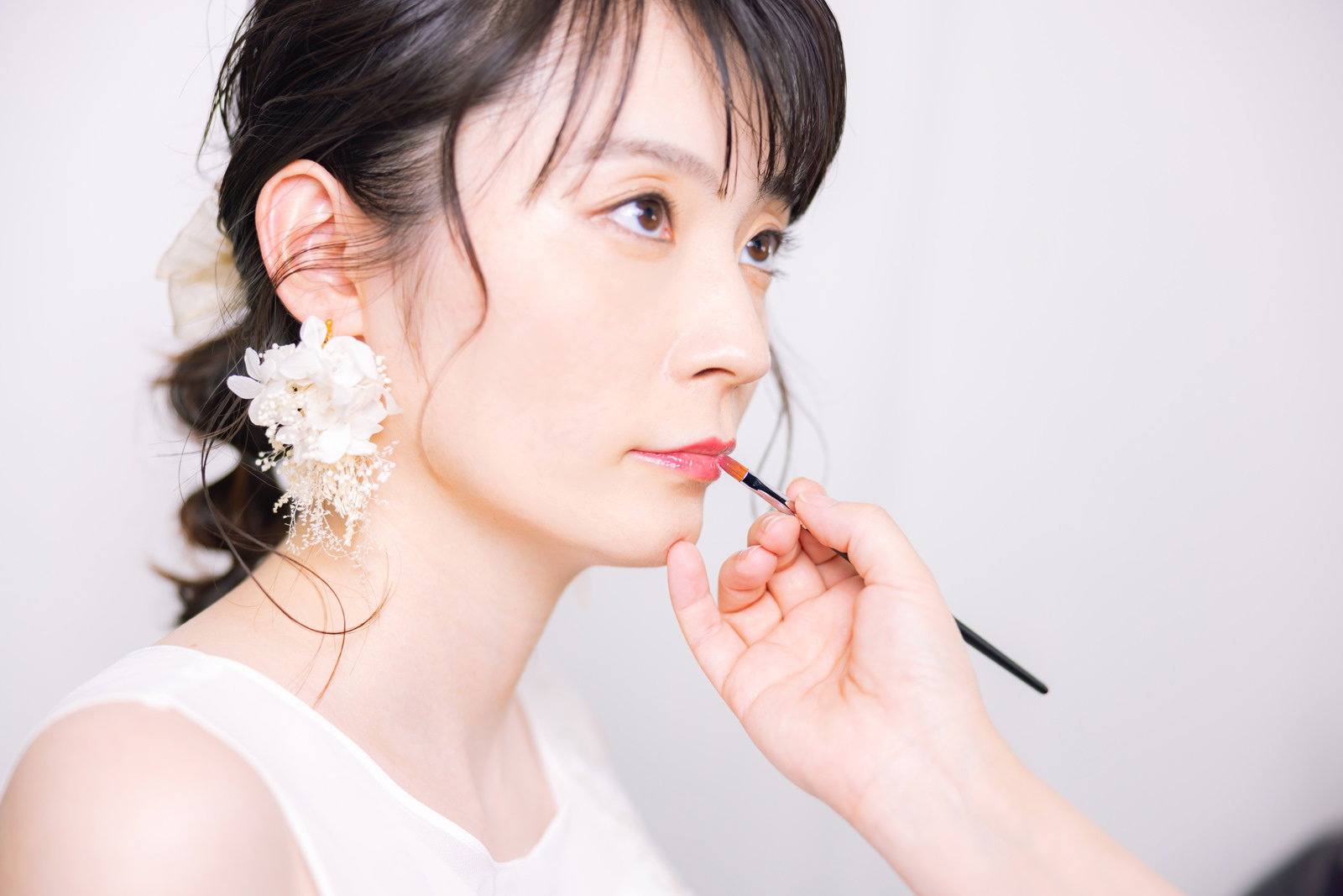 白いウェディングドレスを着た花嫁がリップメイクをしている様子［モデル：たけべともこ］