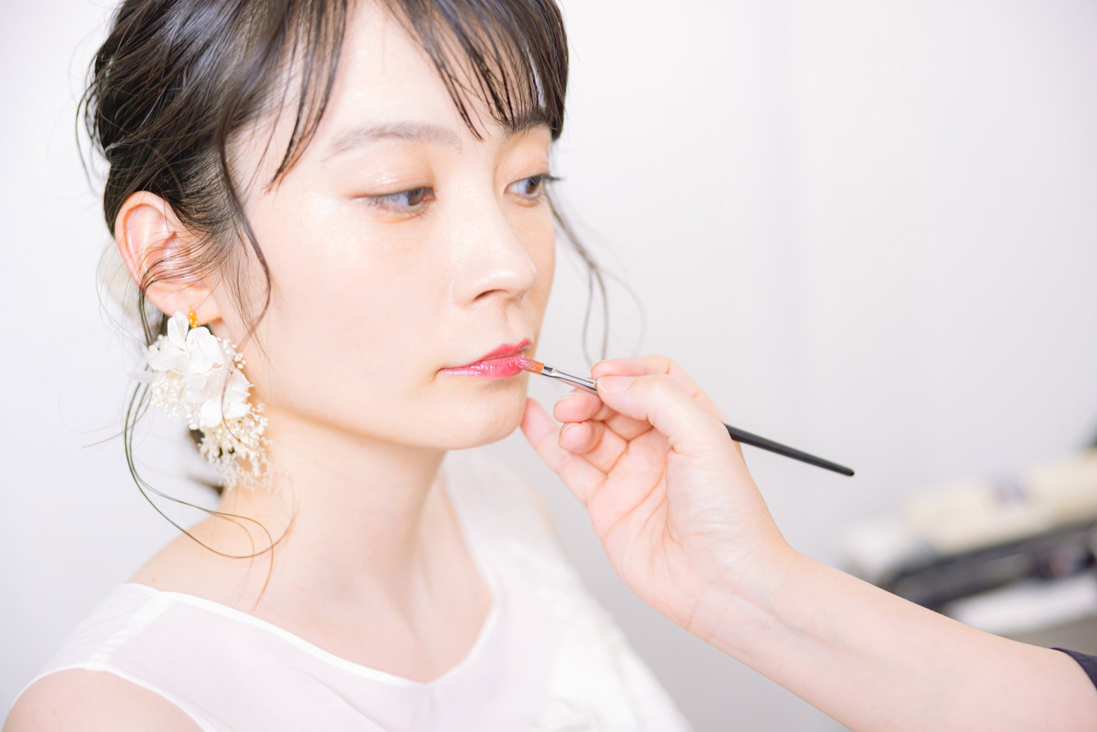 白いウェディングドレス姿の花嫁がリップブラシで口元の化粧直しをしている［モデル：たけべともこ］