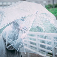 透明なビニール傘を盾に雨の中を進む女性の雨の日の風景の写真