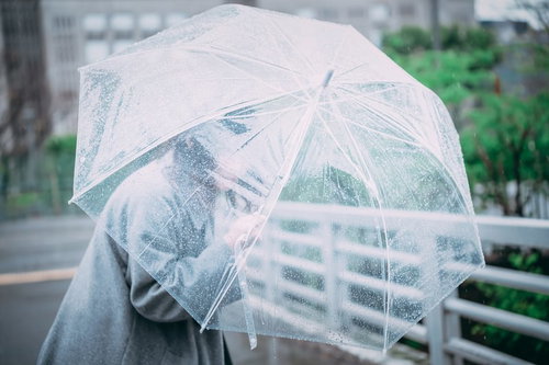 透明なビニール傘を盾に雨の中を進む女性の雨の日の風景