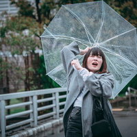 風に飛ばされそうな透明なビニール傘を持つ女性の写真