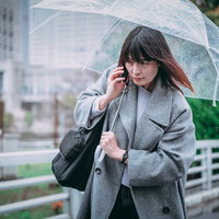 ビニール傘を差しながらスマートフォンで通話する女性の写真