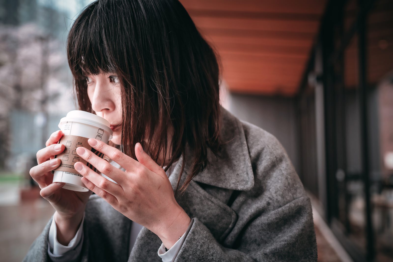 カフェでホットコーヒーを両手で持ちながら飲む女性［モデル：たけべともこ］