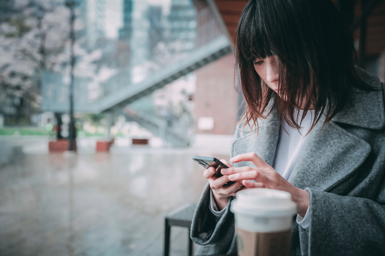 カフェの窓際でスマートフォンを見つめる女性［モデル：たけべともこ］
