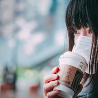 マスク越しにホットコーヒーの香りを楽しむ女性の写真