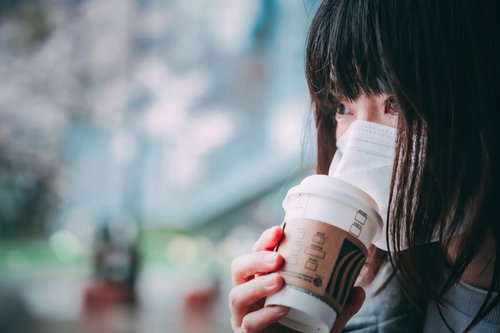 マスク越しにホットコーヒーの香りを楽しむ女性