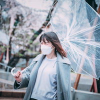 強風でビニール傘が裏返ってしまう女性のマスク着用者の写真