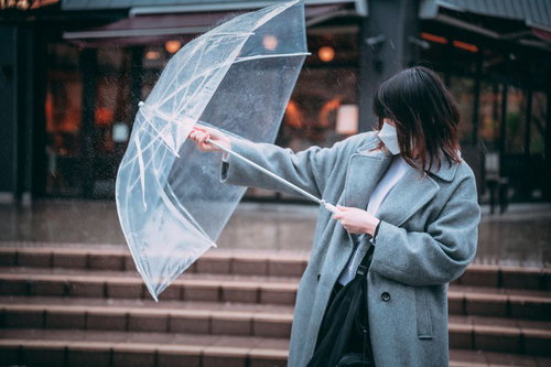 前方からの激しい雨にビニール傘で立ち向かう通勤中の女性