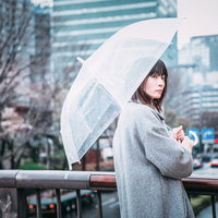 ビニール傘を差して駅前で待ち合わせする女性の写真