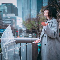 雨が止んだか確かめるビニール傘を持つグレーコートの女性の写真