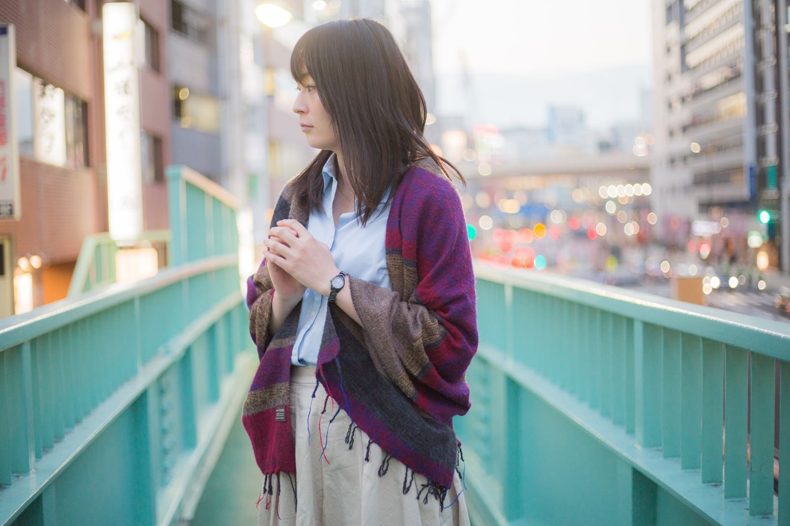 歩道橋の上で景色を眺める、紫色のストールを着た女性［モデル：たけべともこ］