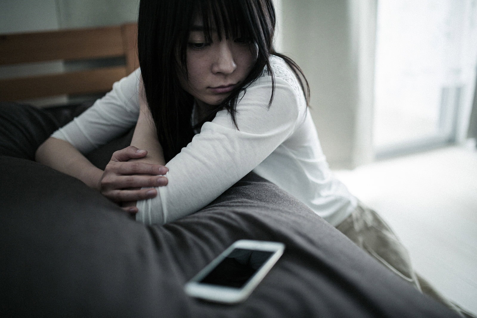 床に座ってうつむく女性とスマートフォン［モデル：たけべともこ］