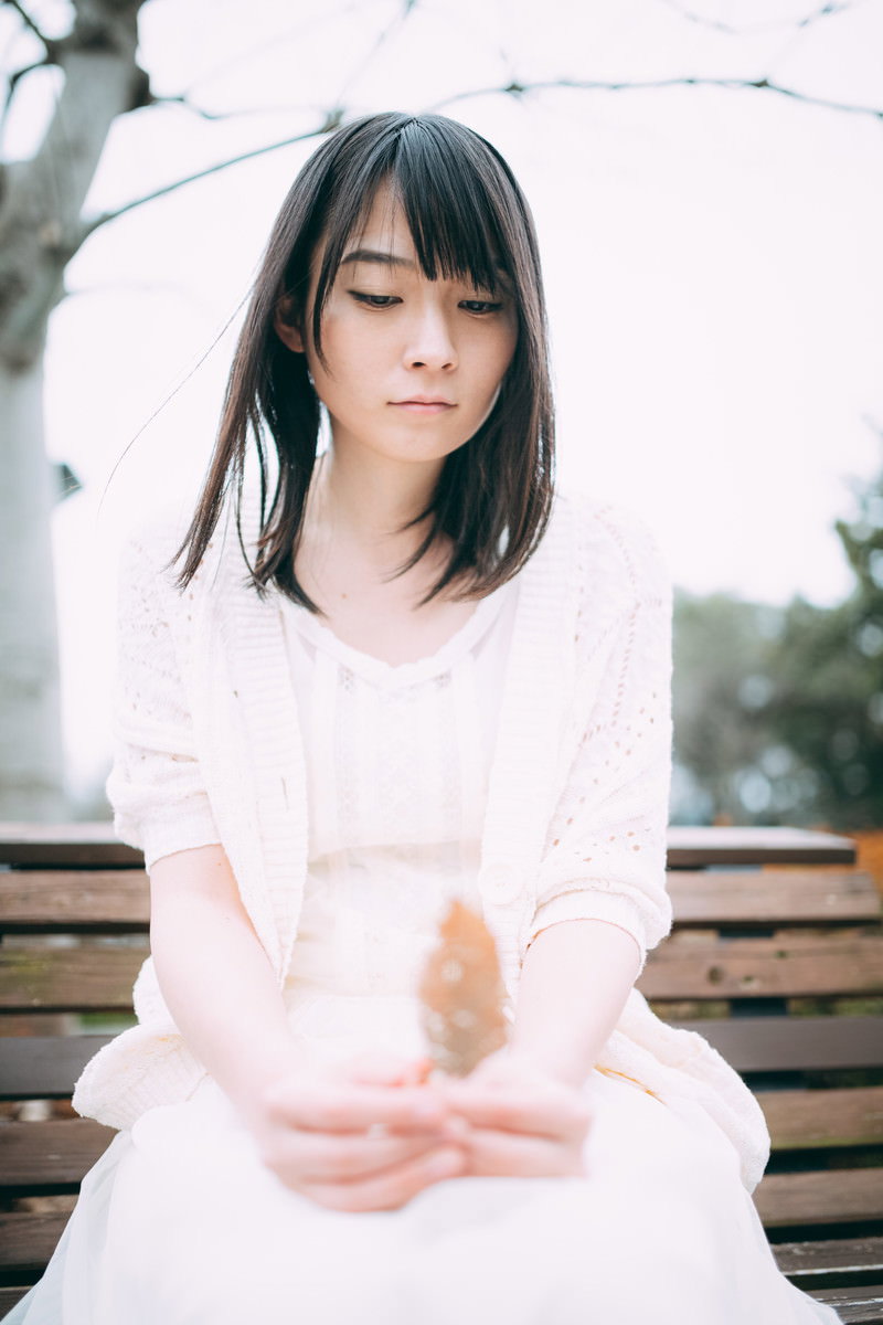 白い服を着てベンチでうつむく女性［モデル：たけべともこ］