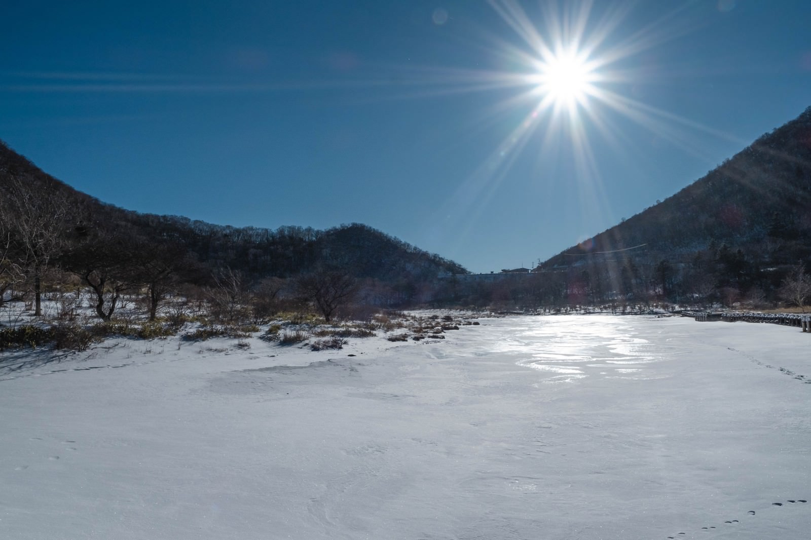 赤城山覚満淵の雪原に強い日差しが降り注ぐ冬の風景