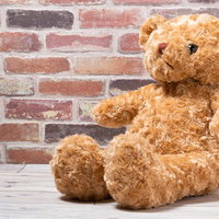 レンガ壁の前に座る茶色のクマのぬいぐるみの写真