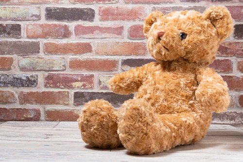 レンガ壁の前に座る茶色のクマのぬいぐるみ