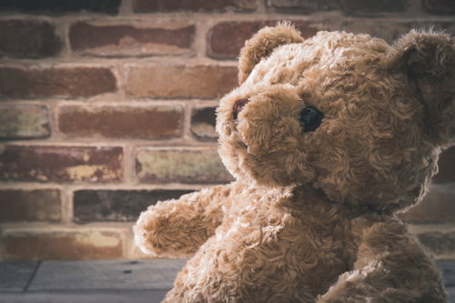 レンガ壁の前に座るシリアスな熊のぬいぐるみ