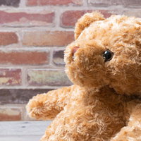 話を聞く茶色のテディベア、レンガ壁の前で座るぬいぐるみの写真