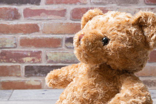 話を聞く茶色のテディベア、レンガ壁の前で座るぬいぐるみ