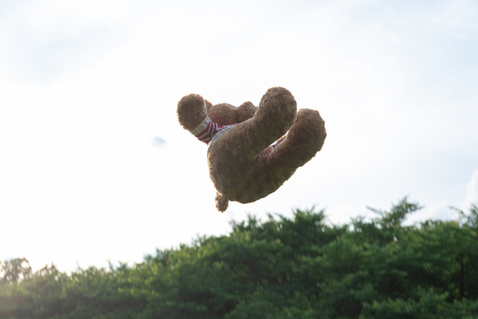 青空の下で宙に浮くくまのぬいぐるみ