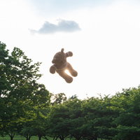 青空と雲を背景に空中を浮かぶクマのぬいぐるみの写真