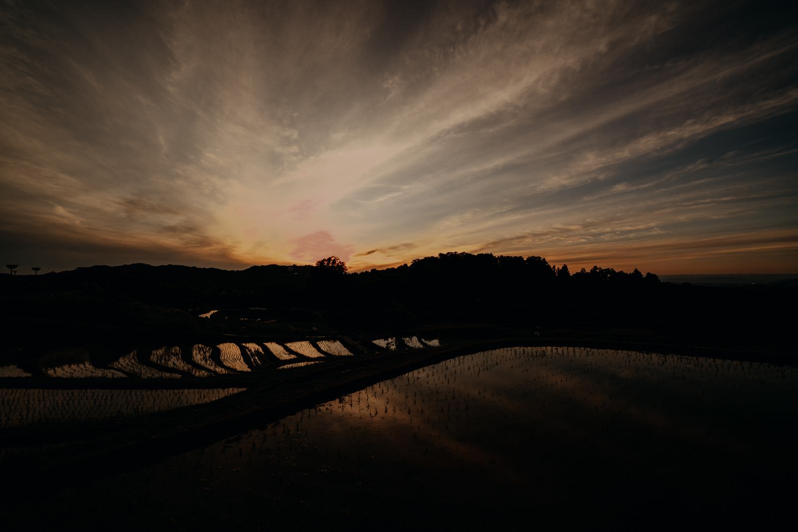 港湾の工業施設と橋を背景に太陽が水面へ沈む夕景
